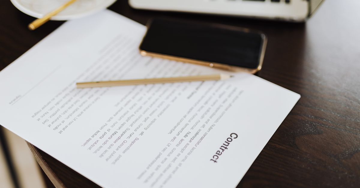 Contrato de diseño web junto a un portátil y documentos de trabajo